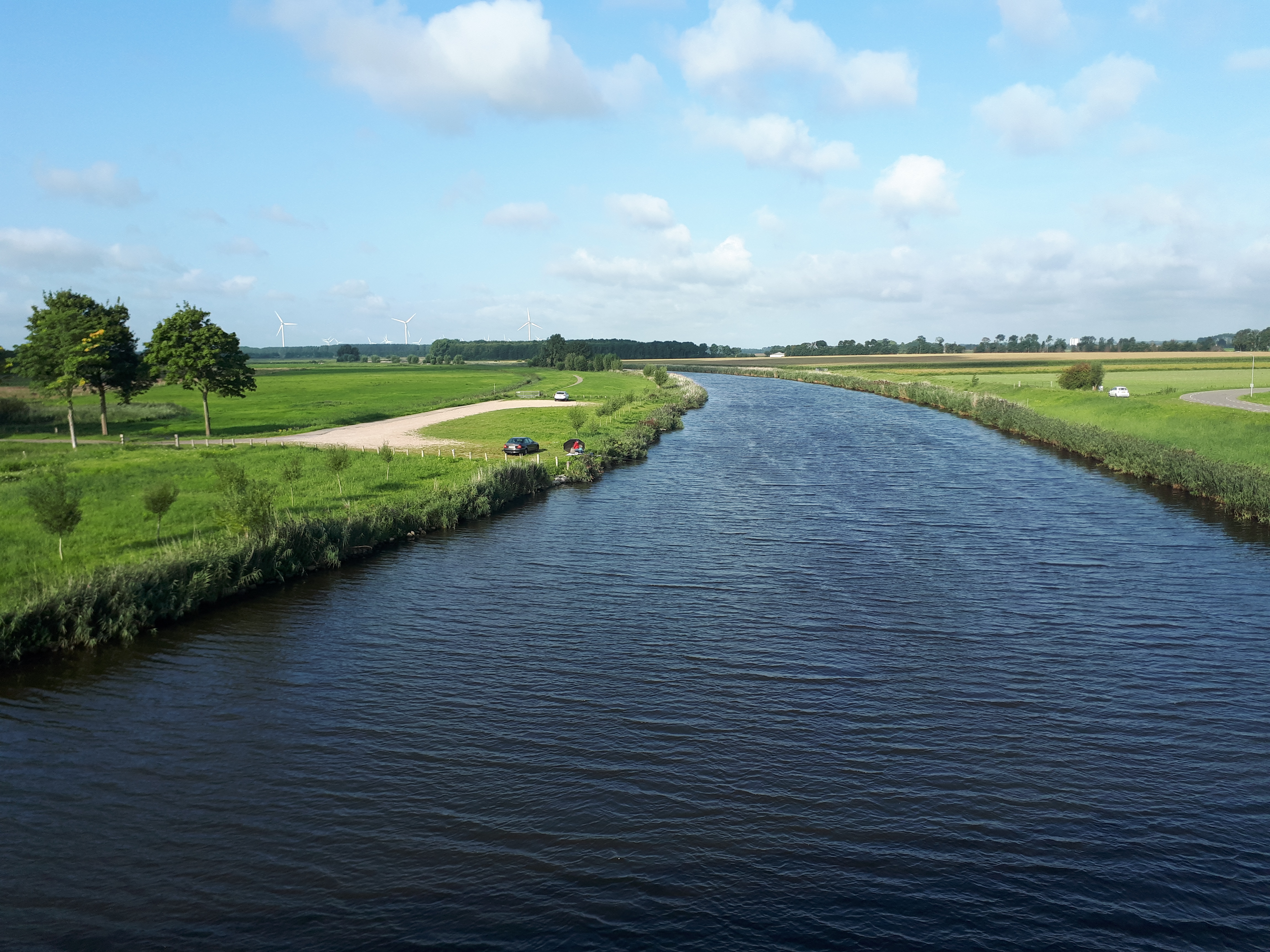 Foto van de Mark of Dintel bij Standdaarbuiten, een breed kronkelend water door een groen polderlandschap met windmolens op de achtergrond.